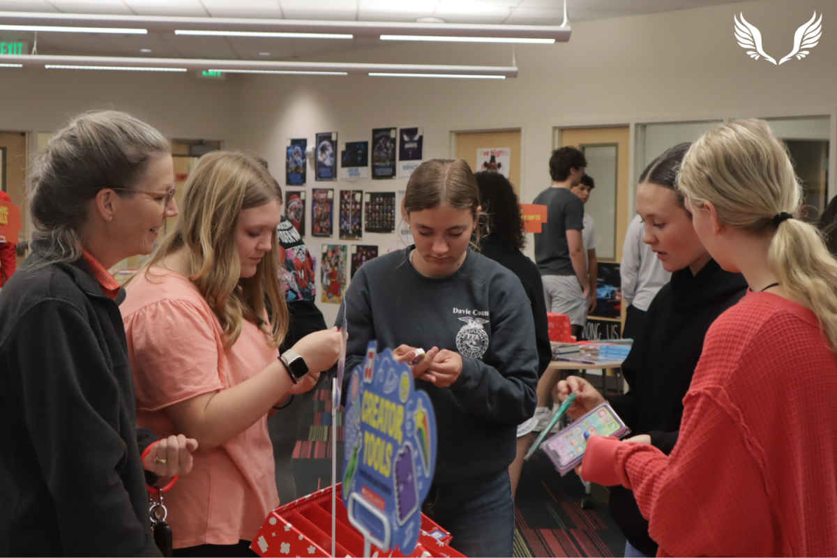 Biology teacher Dr. Georgia Taylor looks over a display of custom erasers along with sophomores Brylie Creel and Lyla Sapp at the Scholastic Book Fair.
