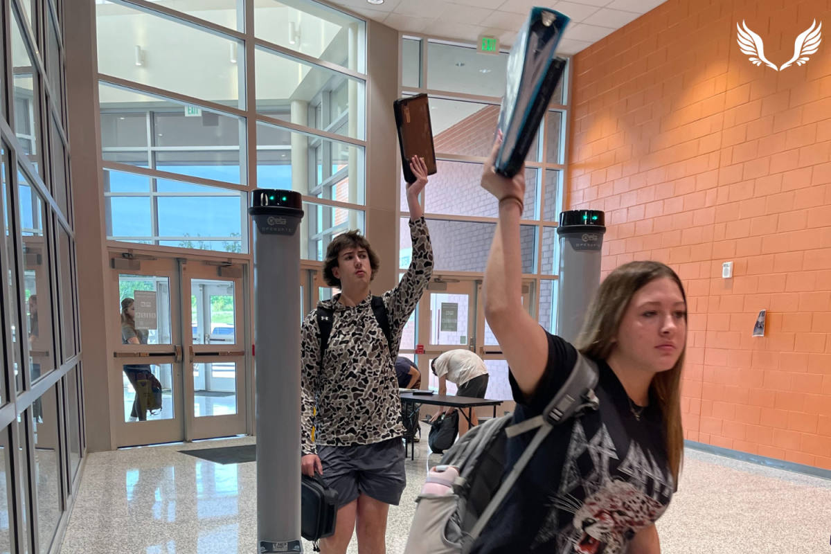 Two Davie students hold their Chromebooks over their heads as they walk through the OpenGate metal detectors. This new procedure has sped up the process of students moving through the metal detectors in the mornings.