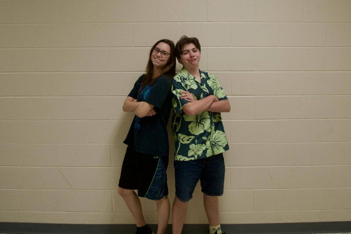 Junior Raina Calhoun and Marshall Gager stand back to back, posing in their Adam Sandler outfits of baggy shorts and fun mismatched shirts.