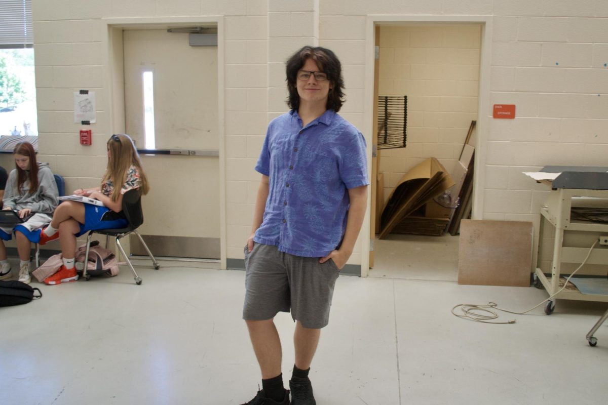 A student poses in the art room in his button up and baggy shorts.