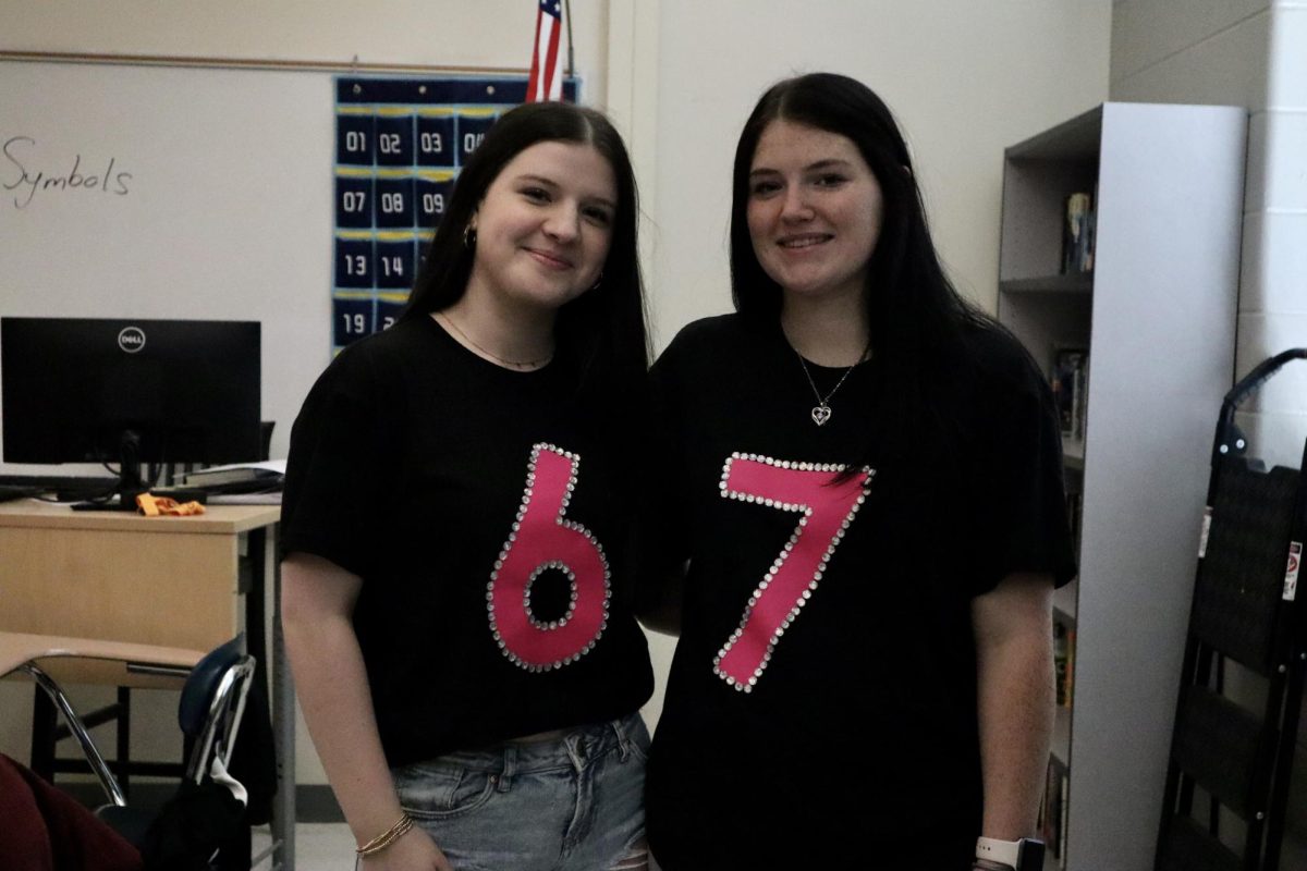 Students Audria Bledsoe and Breanna Surrat stand in Matt Barker’s class in their twinning shirts and jeans, making a funny joke out of the numbers six and seven.