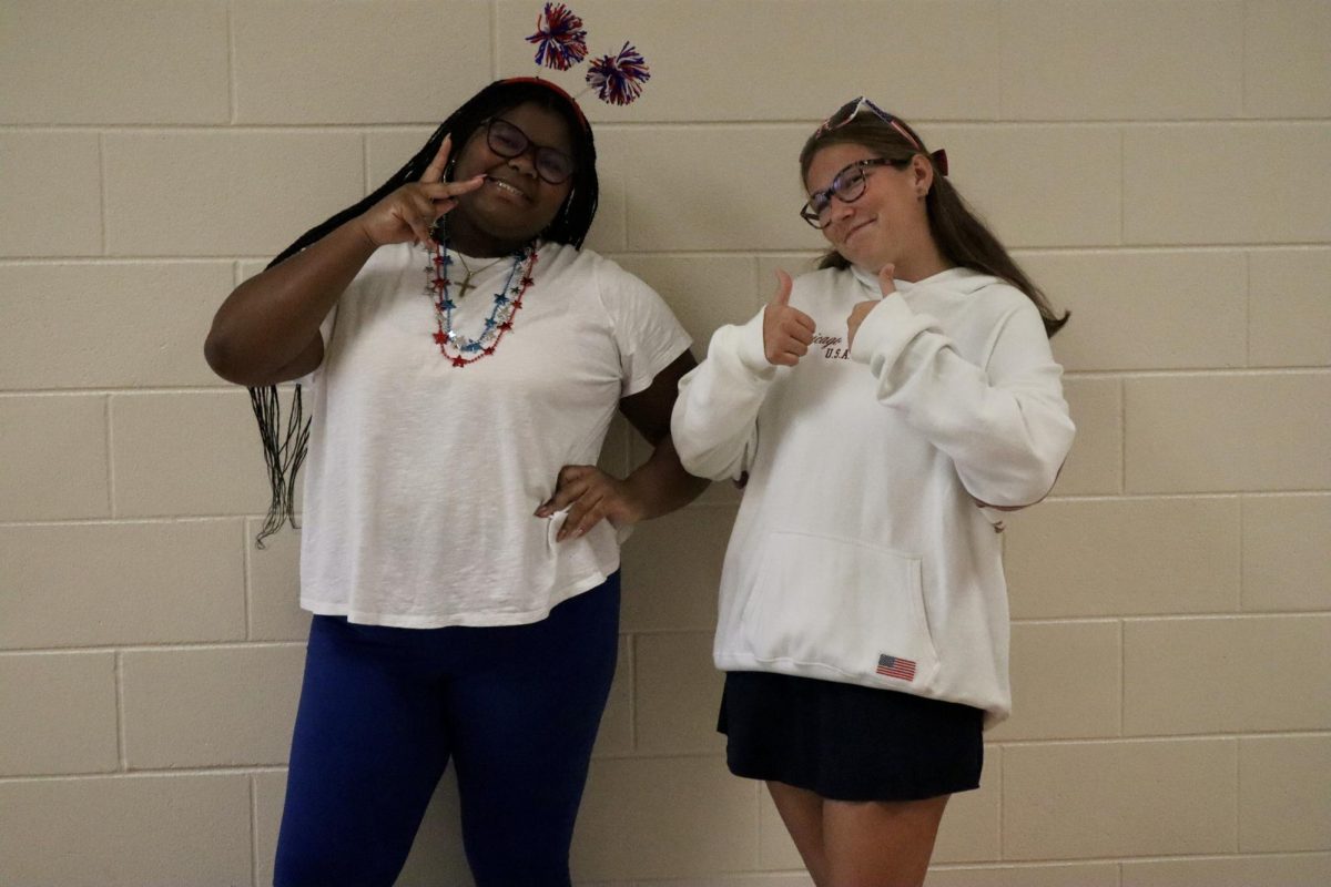 Senior Ava Gary and Junior Evie Conlin are holding up peace signs and thumbs up in their best USA outfits.