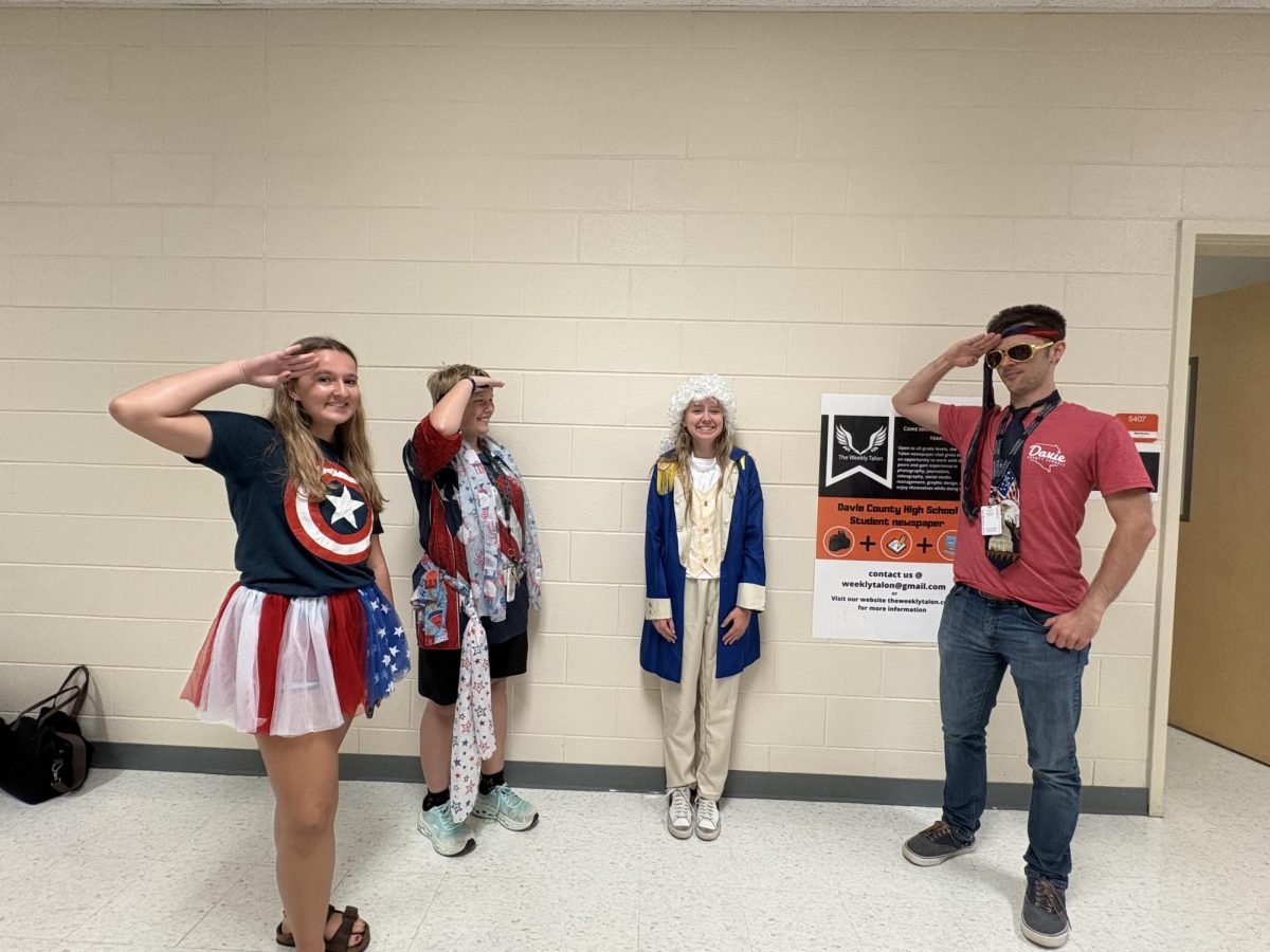 English teacher Matt Barker, junior Hayden Smith, and senior Ace Rucker stand saluting sophomore Kenzie Turner dressed in a George Washington costume. 