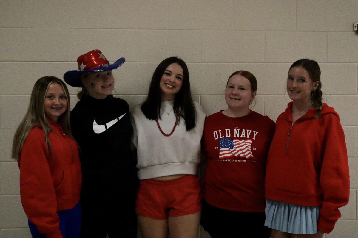 A group of girls stand in the hallway with their arms wrapped around each other rocking their red white and blue.