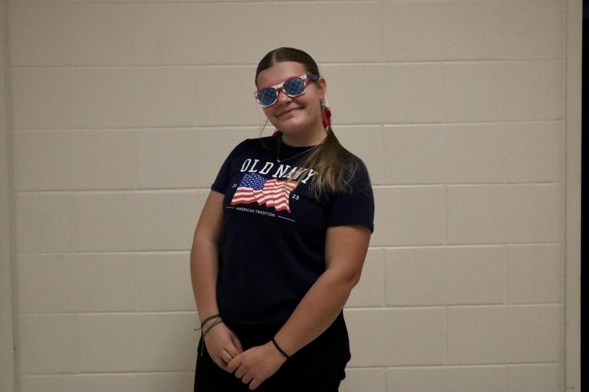 Sophomore Ellie Wallace stands wearing a pair of patriotic sunglasses and an Old Navy Fourth of July shirt. 