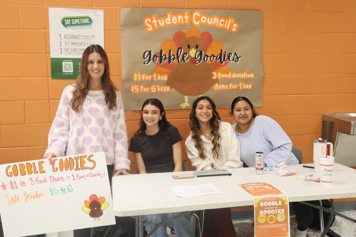 Teacher Laura Doub and seniors Clara Phelps, Emily Bueno, and Daniela Hernandez sit at the Gobble Goodies table waiting for students to buy candy bags.