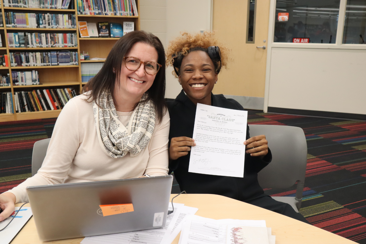 English teacher Ashley Snider sits next to senior Scotlyn Pettigrew who is showing off her letter from Santa. Pettigrew has written this letter to a child as part of Snider's "Letters from Santa" project.