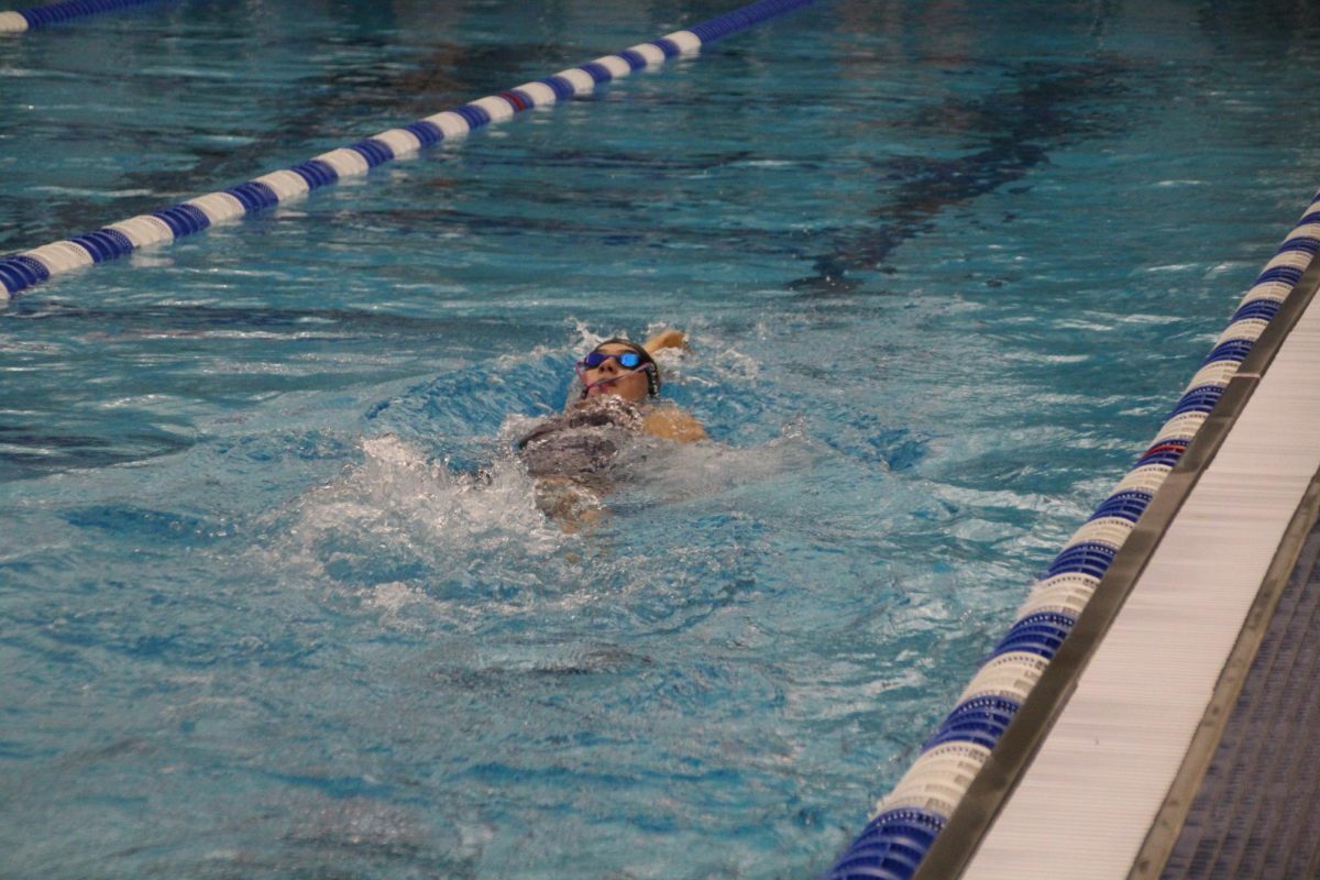 Freshman Addison Cline swims her way through the 100 back, with her goggles half way off her head. 