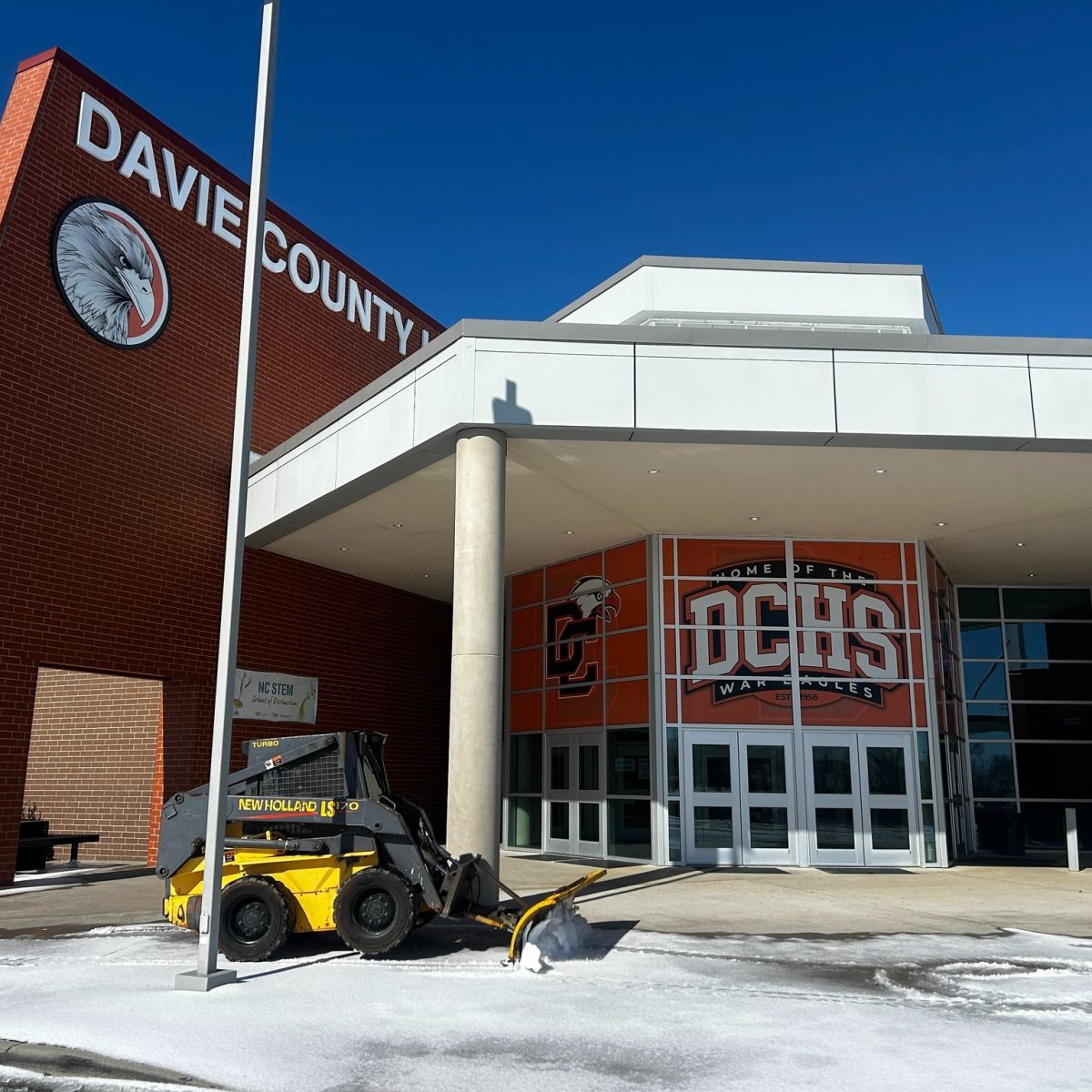 A plow clears snow from the sidewalk in front of the entrance to Davie County High School on January 27. Two back-to-back snow and ice storms led to the district exhausting its allotment of five remote instructional days and cancelling school on four separate occasions in two weeks. | Photo courtesy Davie County Schools