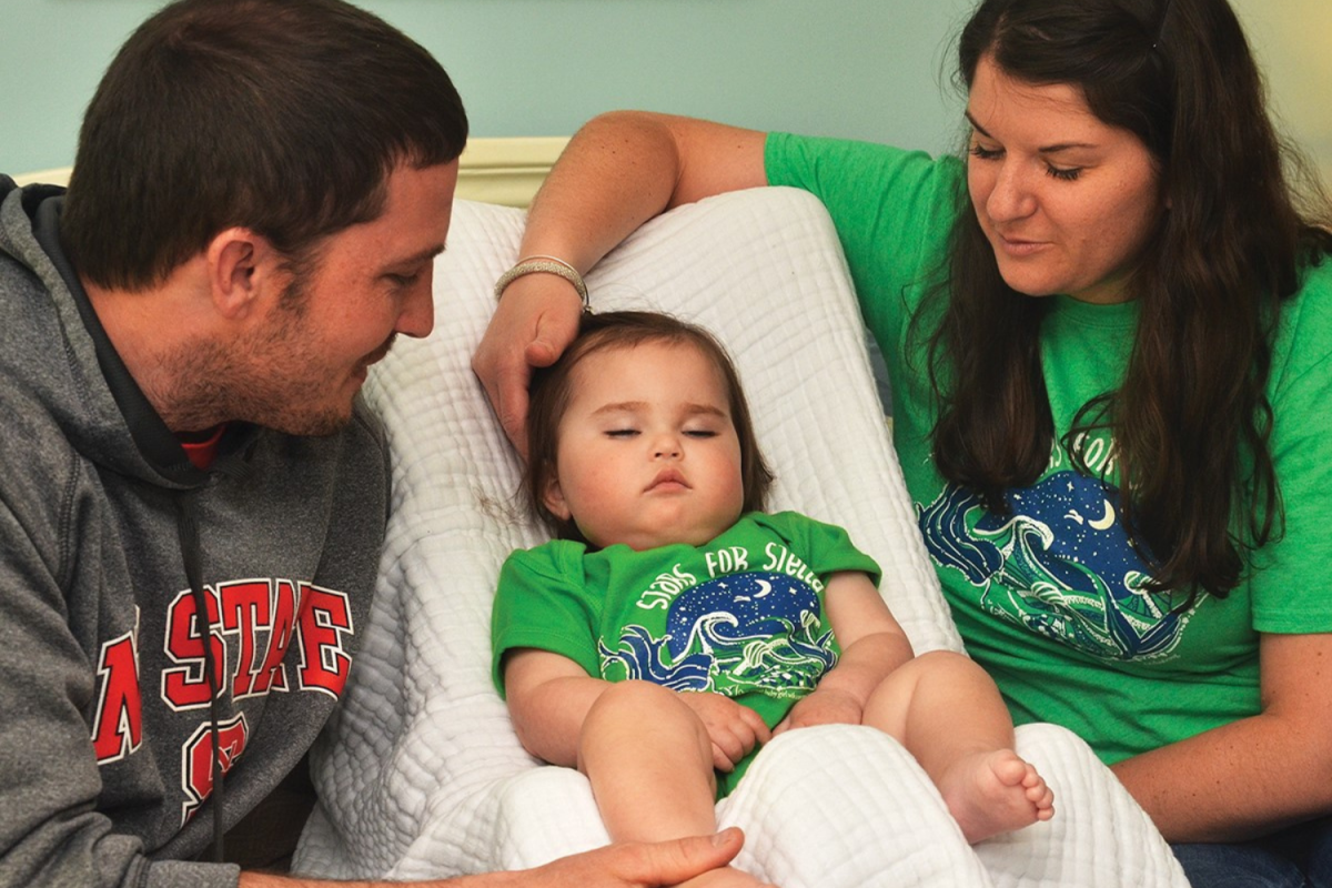 DCHS teachers Jesse and Mindy Ledbetter sit on either side of their daughter. Both Stella and her mother wear a "Stars for Stella" t-shirt. Originally made for their family, the shirts would go on to be sold to support the United Mitochondrial Disease Foundation. | Photo courtesy Mindy Ledbetter