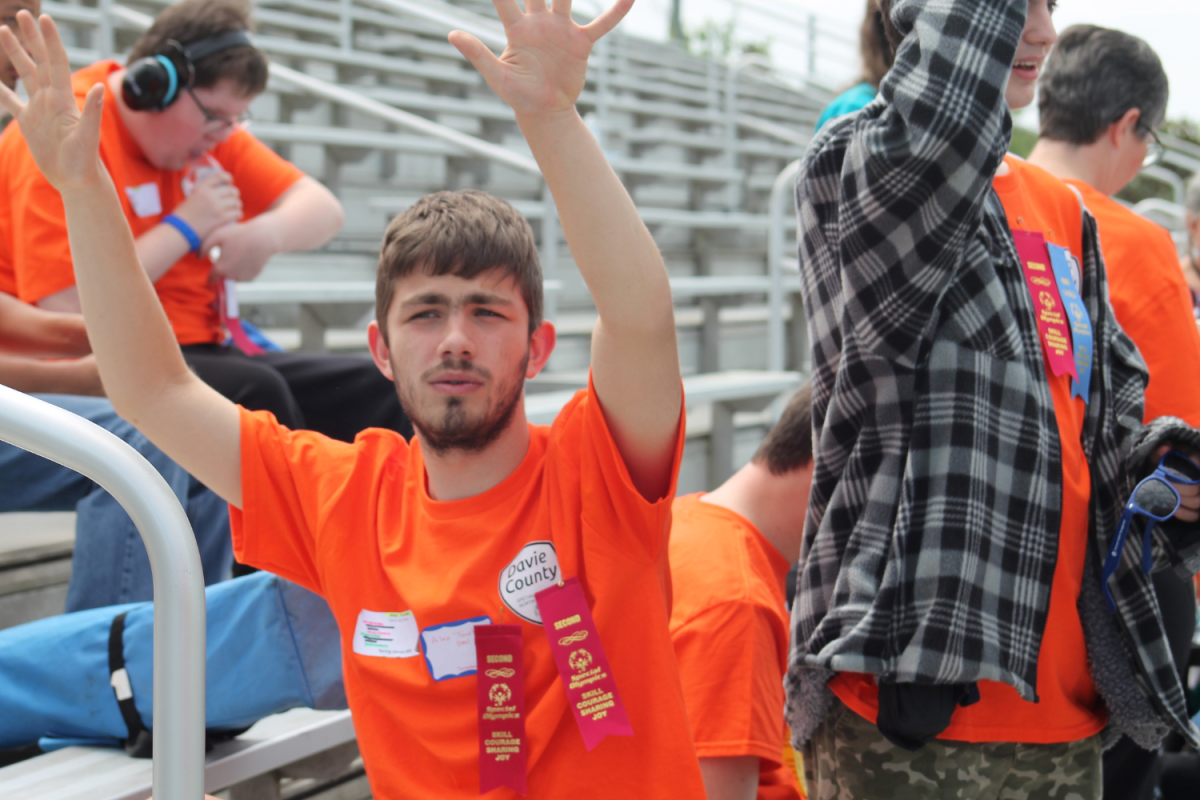 Alex Toburen totes his two second place ribbons as he cheers for others participating in events on the field. Tobuern was one of the few athletes who braved the event of the 400 meter run. 